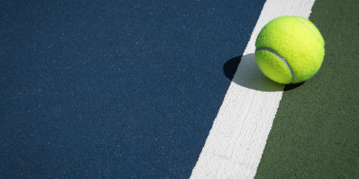 A bright yellow tennis ball resting on a colorful court near a white line