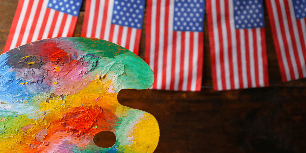 Colorful artist's palette in front of small American flags hanging on a rustic background