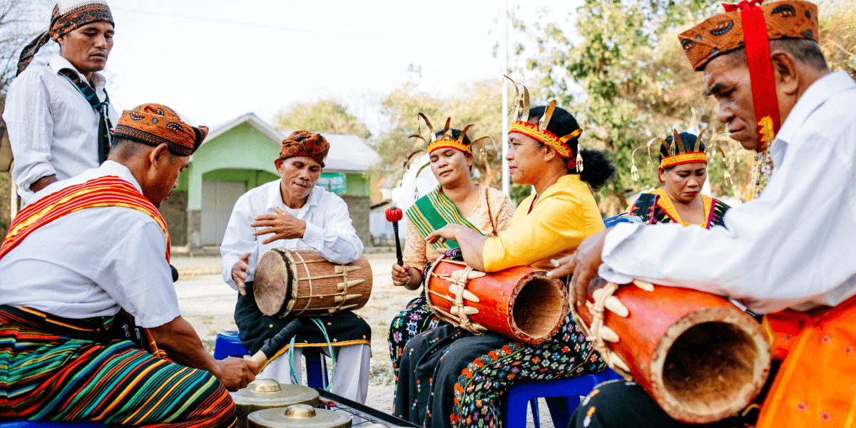 A group of musicians in traditional attire performs with drums and instruments outdoors.