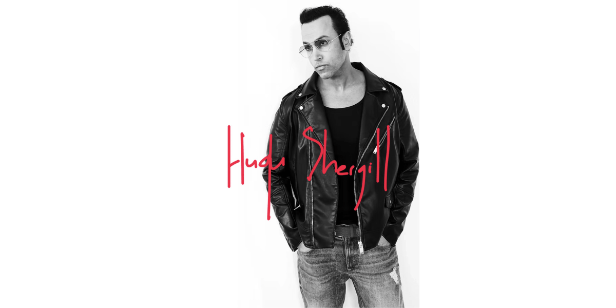 "Black and white portrait of Hugh Shergill wearing a leather jacket and sunglasses with a red handwritten signature of his name, Hugh Shergill, below the image."