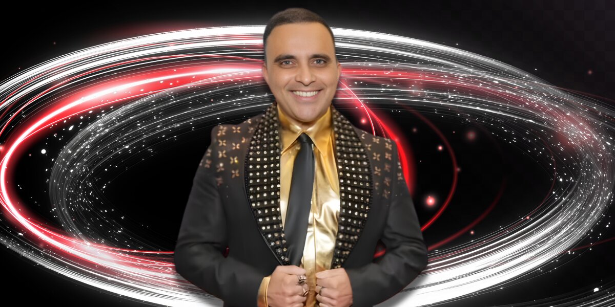 Smiling man in a studded black suit and gold shirt stands confidently. Behind him, swirls of red and white lights create a dynamic, energetic backdrop.