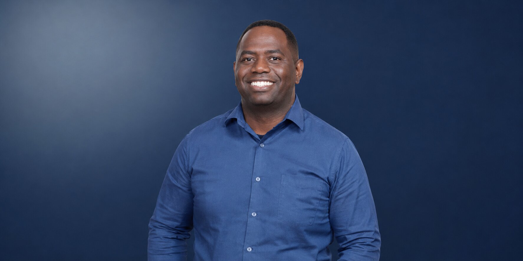 Smiling man in blue button-down shirt against dark blue background, accompanying article about podcast host fostering authentic conversations.