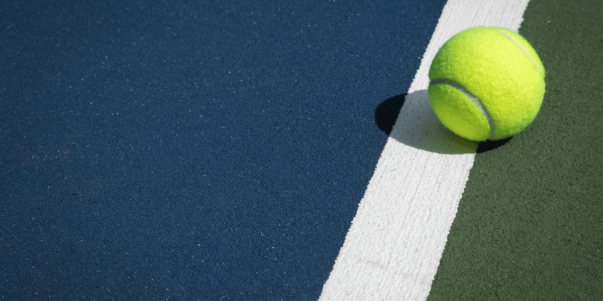 A bright yellow tennis ball resting on a colorful court near a white line