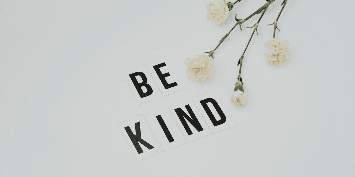 Flat lay of white flowers and letter tiles spelling "BE KIND" on a light background