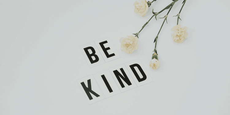 Flat lay of white flowers and letter tiles spelling "BE KIND" on a light background