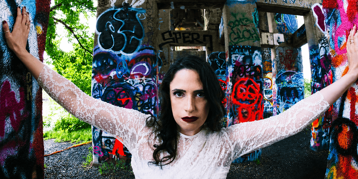 A woman in a white dress poses against colorful graffiti-covered pillars outdoors