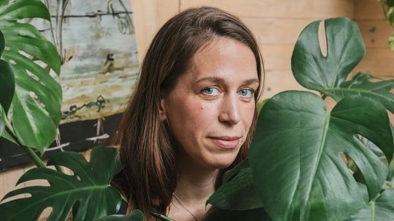 Portrait of artist Laila Seidel surrounded by large green leaves.