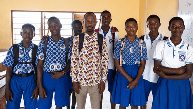 Dacosta Aheto stands with students in school uniforms inside a classroom in Ghana.