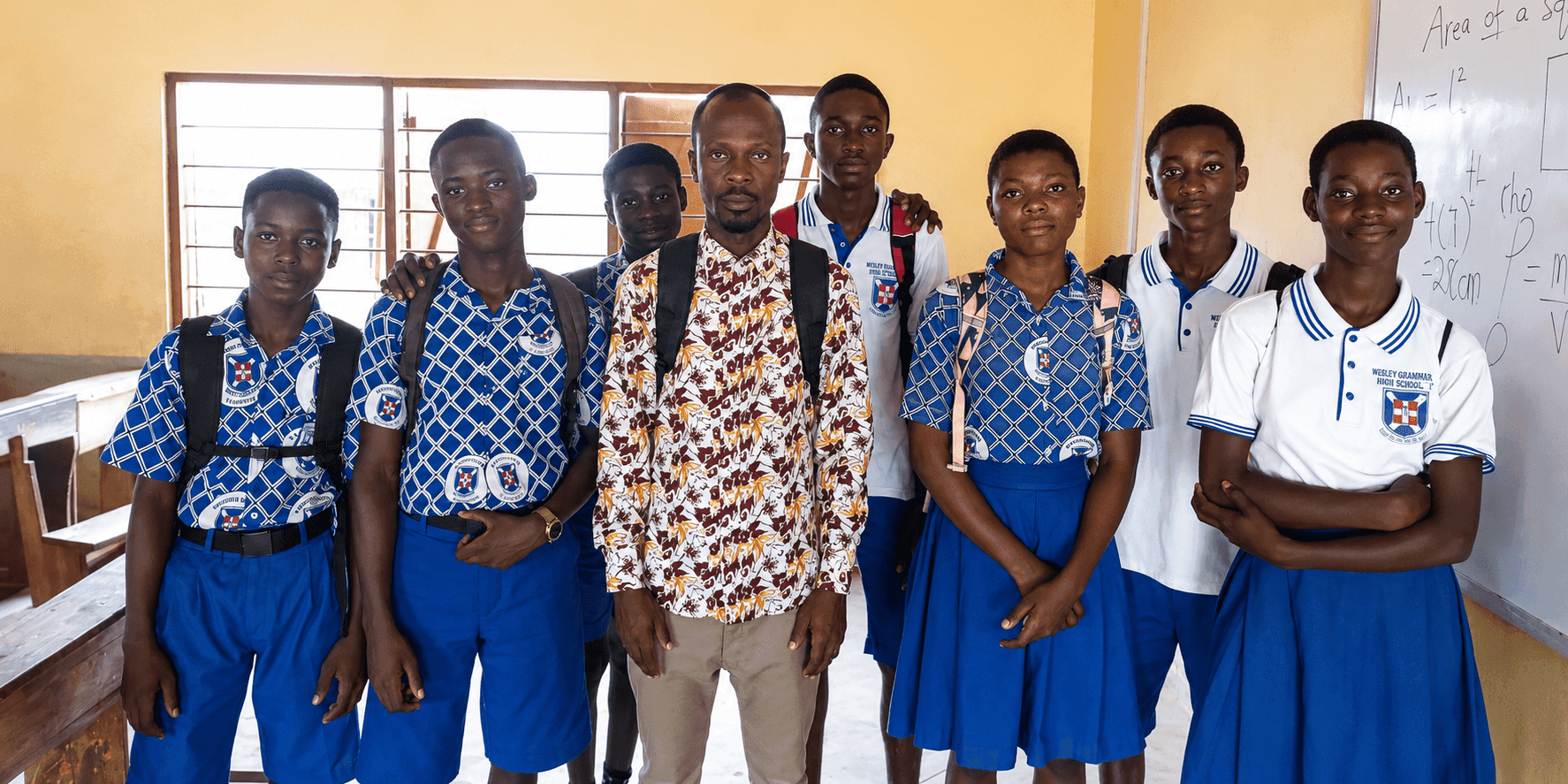 Dacosta Aheto stands with students in school uniforms inside a classroom in Ghana.