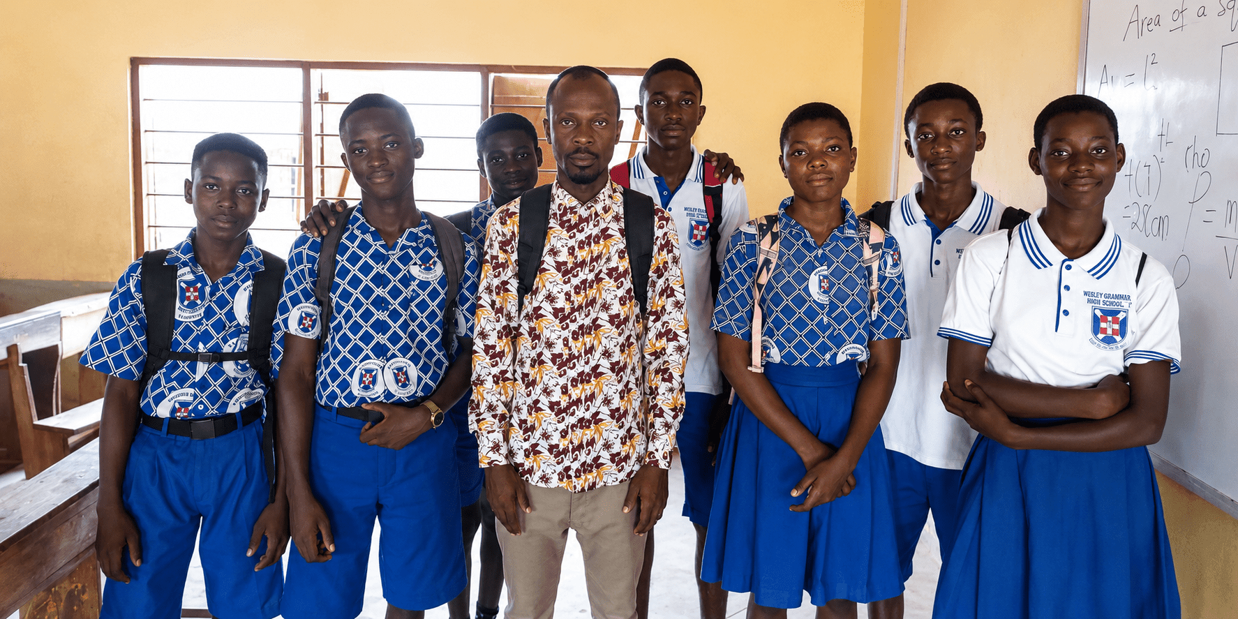 Dacosta Aheto stands with students in school uniforms inside a classroom in Ghana.
