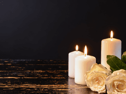 Three white candles and two white roses on a dark wooden surface