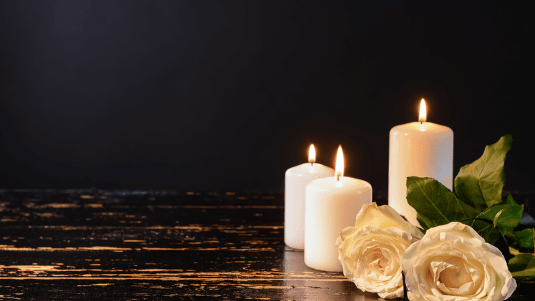 Three white candles and two white roses on a dark wooden surface