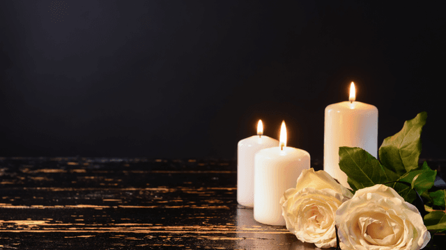 Three white candles and two white roses on a dark wooden surface