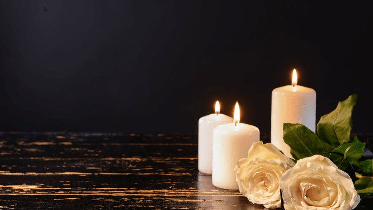 Three white candles and two white roses on a dark wooden surface