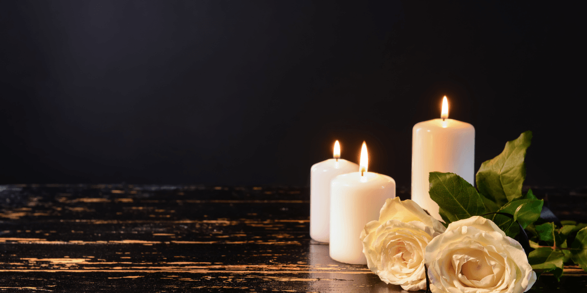Three white candles and two white roses on a dark wooden surface