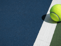 A bright yellow tennis ball resting on a colorful court near a white line