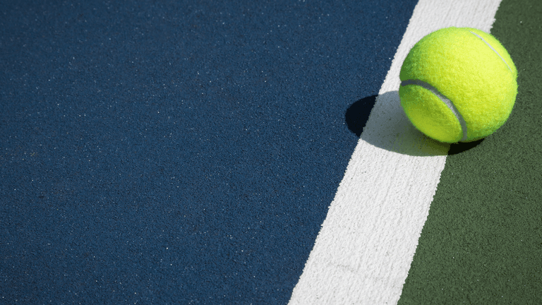 A bright yellow tennis ball resting on a colorful court near a white line