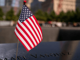Small American flag next to a name on a memorial plaque in remembrance.