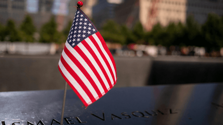 Small American flag next to a name on a memorial plaque in remembrance.