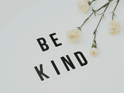 Flat lay of white flowers and letter tiles spelling "BE KIND" on a light background