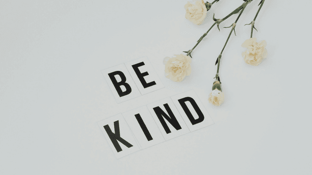 Flat lay of white flowers and letter tiles spelling "BE KIND" on a light background