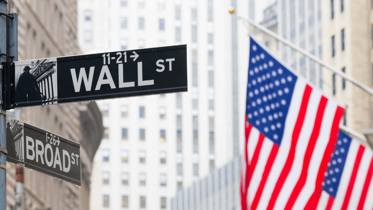 Street signs for Wall Street and Broad Street with an American flag in the background