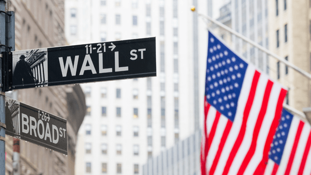 Street signs for Wall Street and Broad Street with an American flag in the background