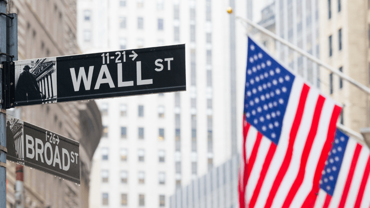 Street signs for Wall Street and Broad Street with an American flag in the background