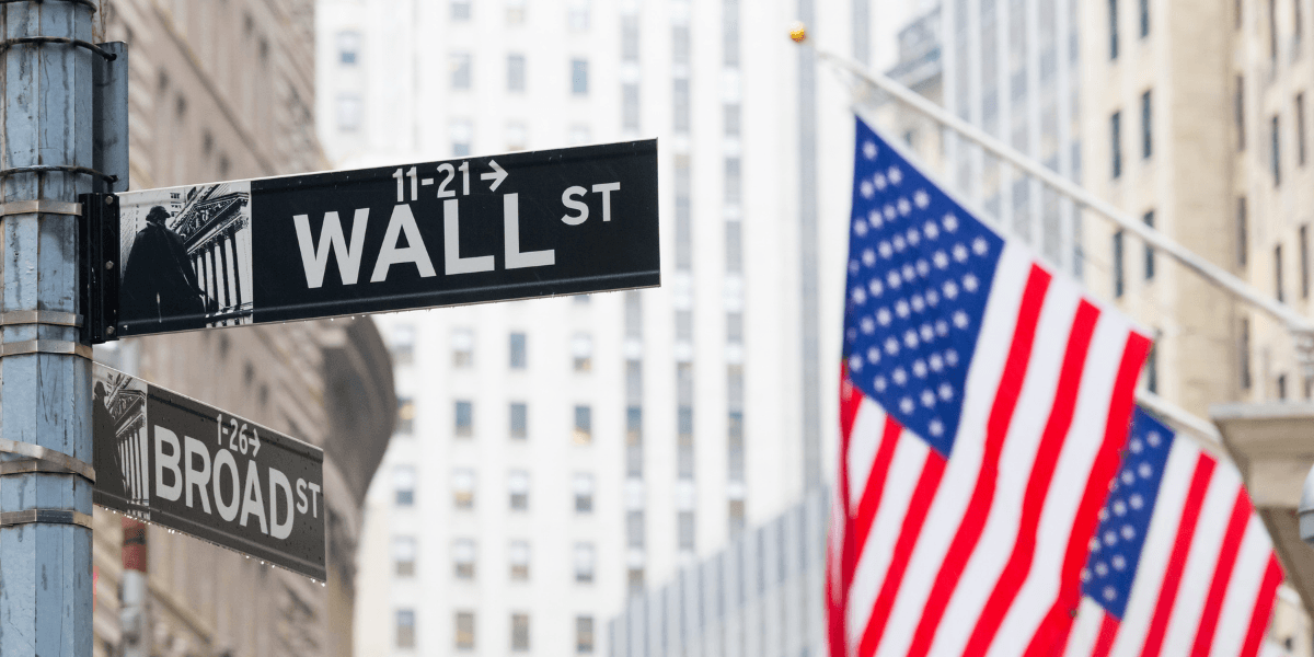 Street signs for Wall Street and Broad Street with an American flag in the background