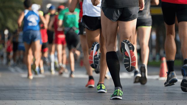 Runners participate in a race on a paved pathway lined with trees