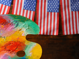 Colorful artist's palette in front of small American flags hanging on a rustic background