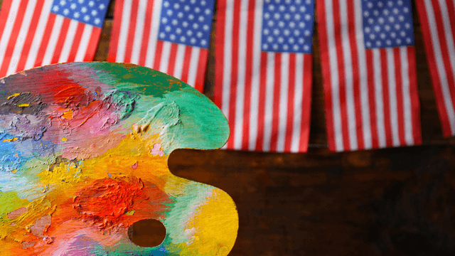 Colorful artist's palette in front of small American flags hanging on a rustic background