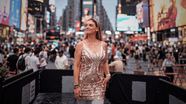 Woman in a sparkling dress standing in a crowded Times Square at dusk