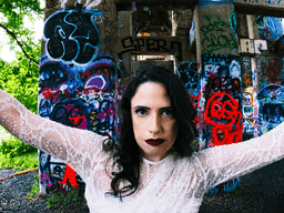 A woman in a white dress poses against colorful graffiti-covered pillars outdoors