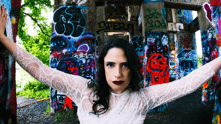A woman in a white dress poses against colorful graffiti-covered pillars outdoors