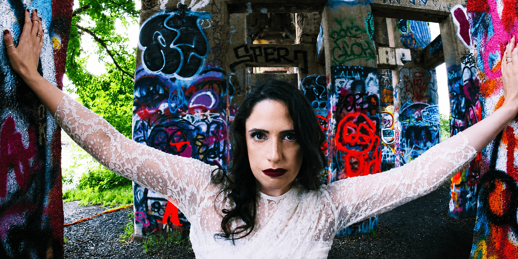 A woman in a white dress poses against colorful graffiti-covered pillars outdoors