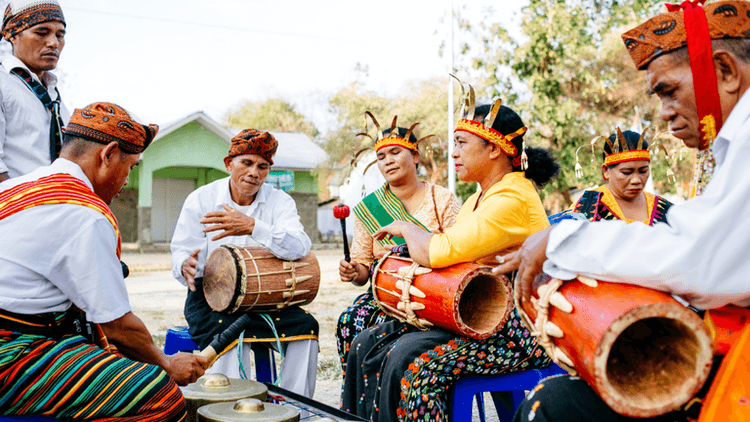 A group of musicians in traditional attire performs with drums and instruments outdoors.