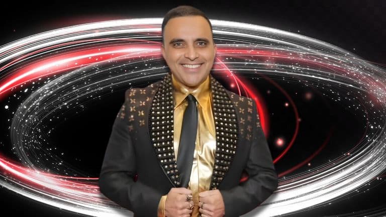 Smiling man in a studded black suit and gold shirt stands confidently. Behind him, swirls of red and white lights create a dynamic, energetic backdrop.