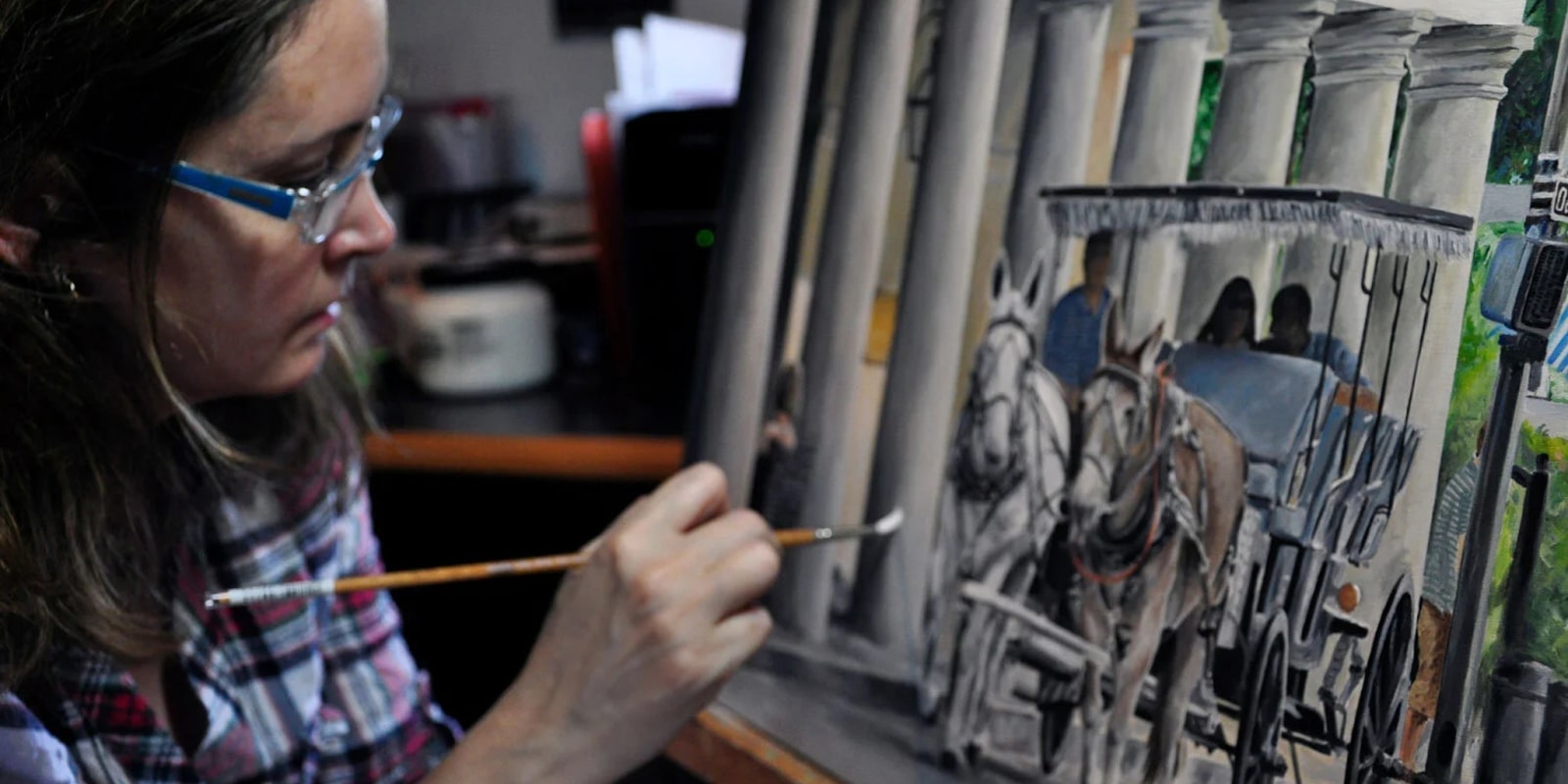 The image shows an artist painting a horse-drawn carriage with a focus on the details of the artwork being created.