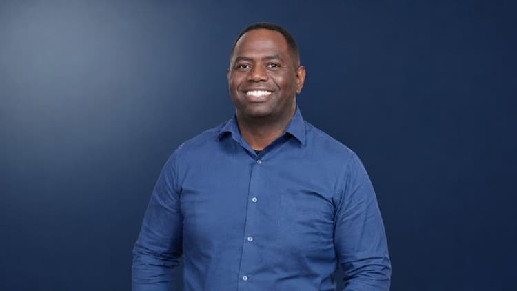 Smiling man in blue button-down shirt against dark blue background, accompanying article about podcast host fostering authentic conversations.