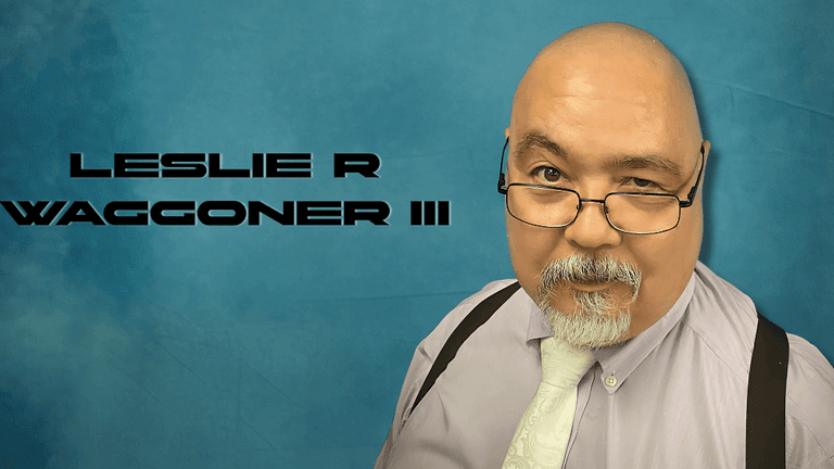 "Portrait of author Leslie R. Waggoner III, dressed in a purple shirt with a tie, sporting glasses and a beard, set against a blue background."