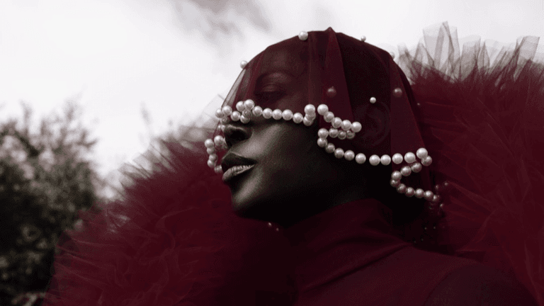 A model wearing a striking red tulle outfit with a pearl-embellished veil, reflecting the bold, cultural storytelling approach of fashion stylist and entrepreneur Jenny Ubebe. This image captures Jenny's signature blend of high fashion, personal heritage, and artistic expression in her work.