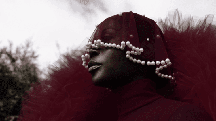 A model wearing a striking red tulle outfit with a pearl-embellished veil, reflecting the bold, cultural storytelling approach of fashion stylist and entrepreneur Jenny Ubebe. This image captures Jenny's signature blend of high fashion, personal heritage, and artistic expression in her work.