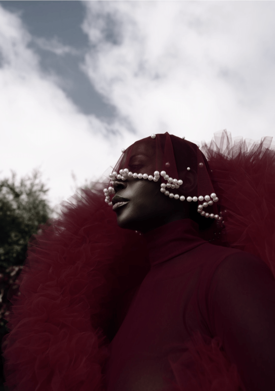 A model wearing a striking red tulle outfit with a pearl-embellished veil, reflecting the bold, cultural storytelling approach of fashion stylist and entrepreneur Jenny Ubebe. This image captures Jenny's signature blend of high fashion, personal heritage, and artistic expression in her work.