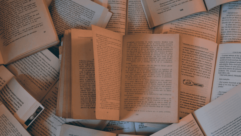 A collection of open books scattered on a surface, displaying pages with text in a warm, soft lighting.