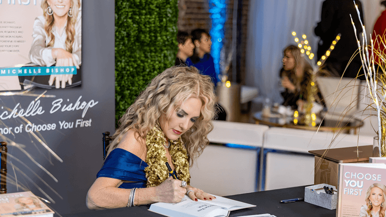 Michelle Bishop signs books at an event, promoting her empowerment journey and message from her bestseller "Choose You First."