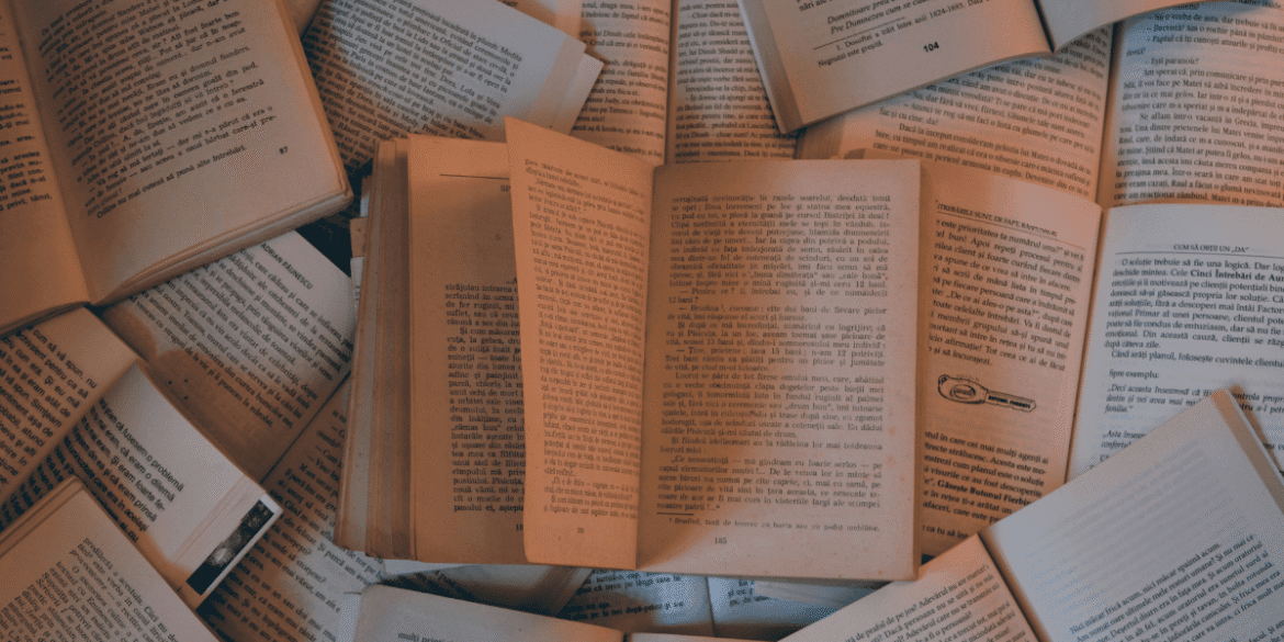 A collection of open books scattered on a surface, displaying pages with text in a warm, soft lighting.