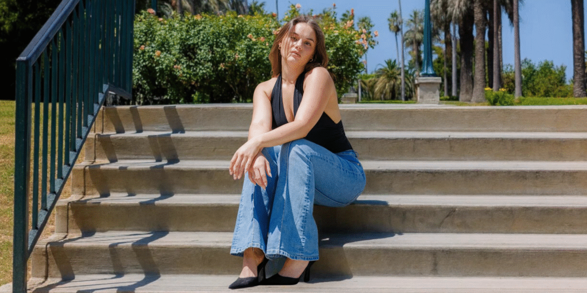 Jessi sitting on outdoor steps in jeans and a black top, representing her relatable, grounded creator persona.