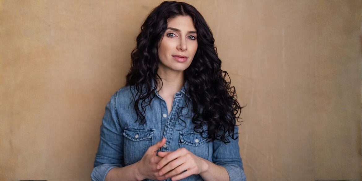 Anabelle Ciancuillo, a woman with long curly hair in a denim shirt, represents emotional storytelling in Hollywood.