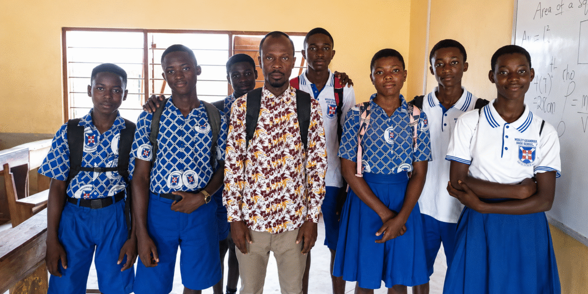 Dacosta Aheto stands with students in school uniforms inside a classroom in Ghana.